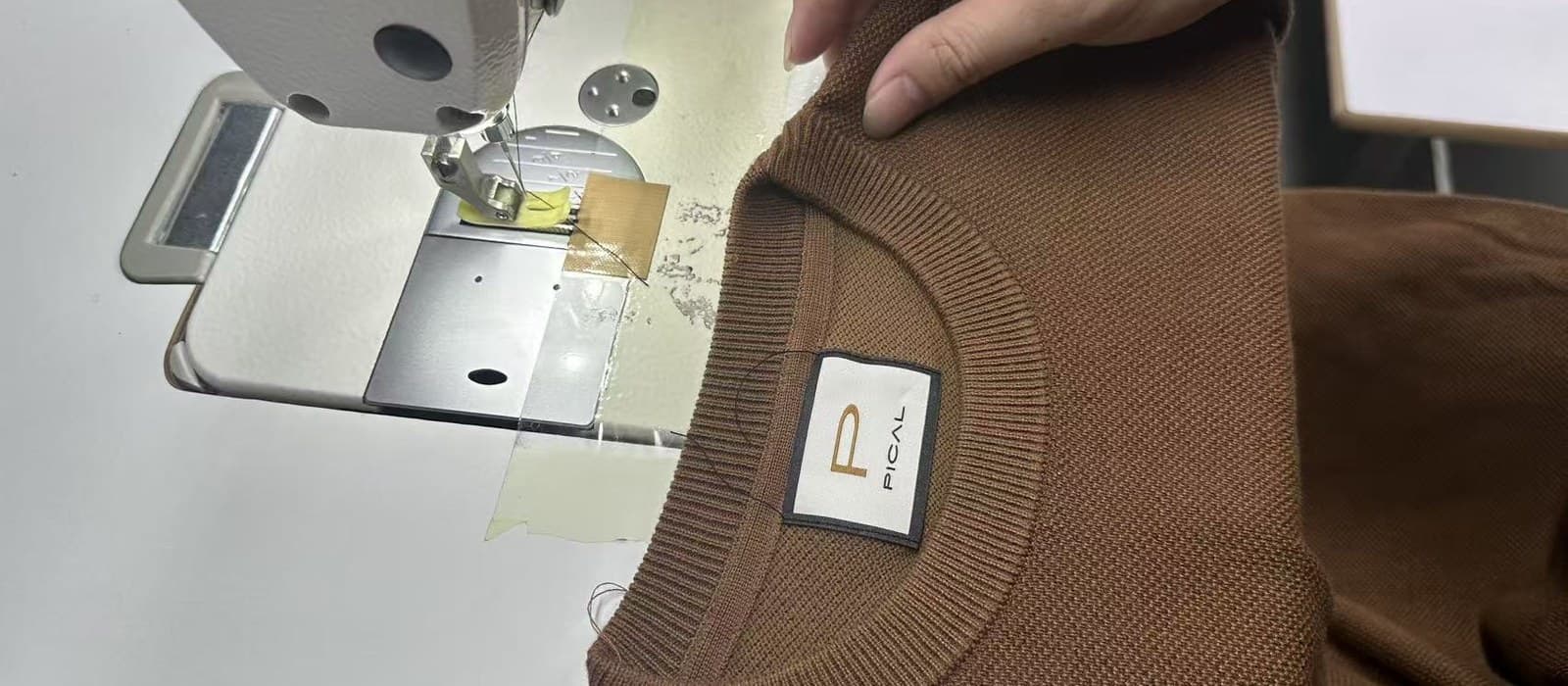 A customer's woven main label being stitched into the neckline of a finished sweater