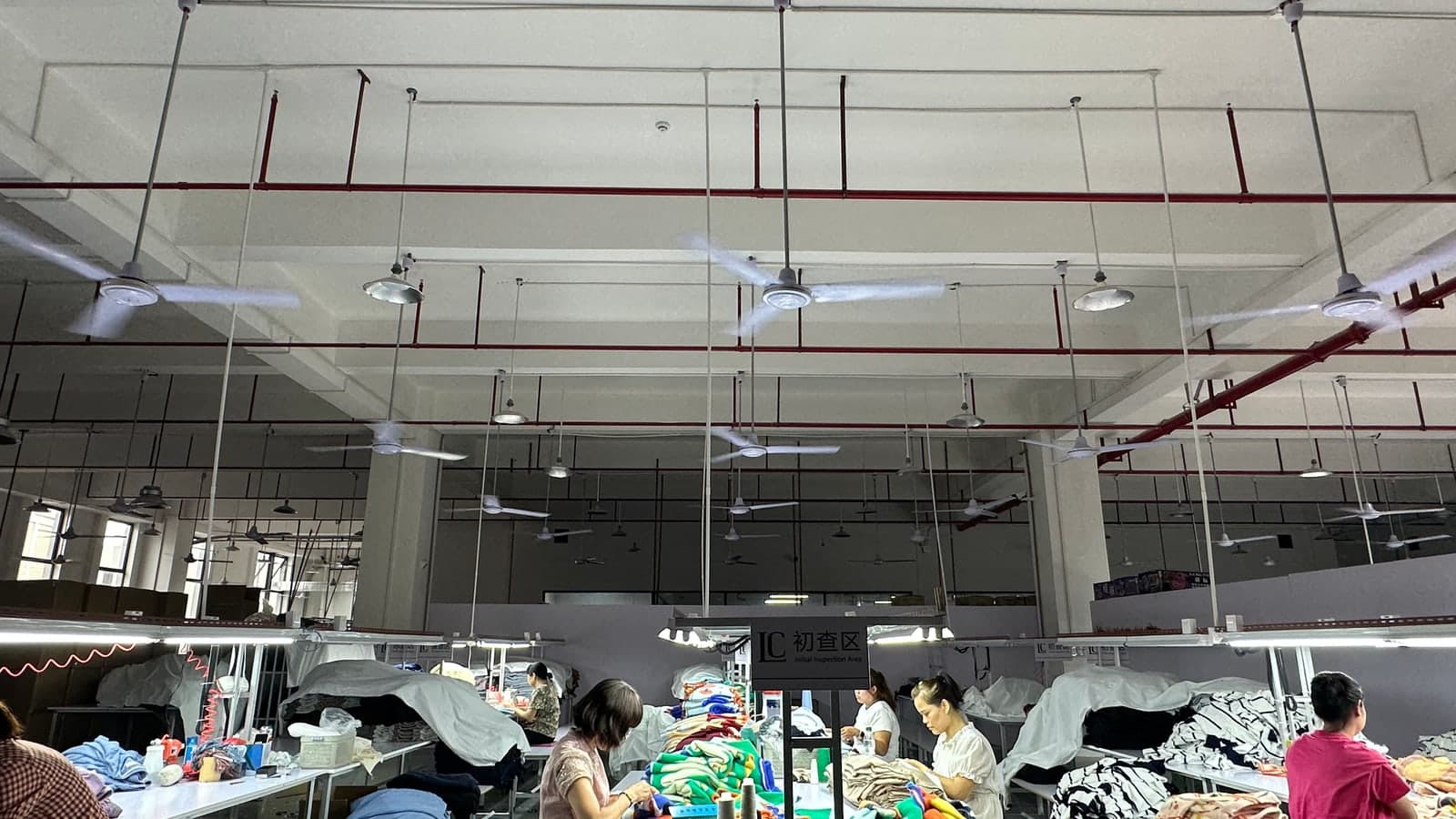 Workers inspecting multicolour knitwear samples at long QC table